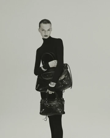 Model in black turtleneck holding two black leather handbags against a neutral studio background by Jonas Bresnan