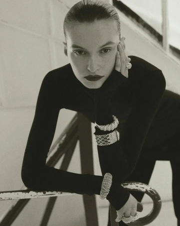 Model wearing dark turtleneck and chunky silver bracelets leaning on a staircase rail, photographed by Jonas Bresnan.
