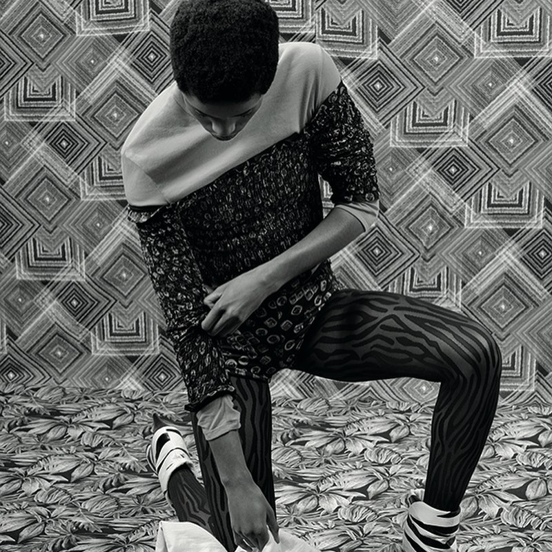 Monochrome fashion shot of a person kneeling on a patterned surface, wearing a patterned top, zebra print tights, and platform shoes.