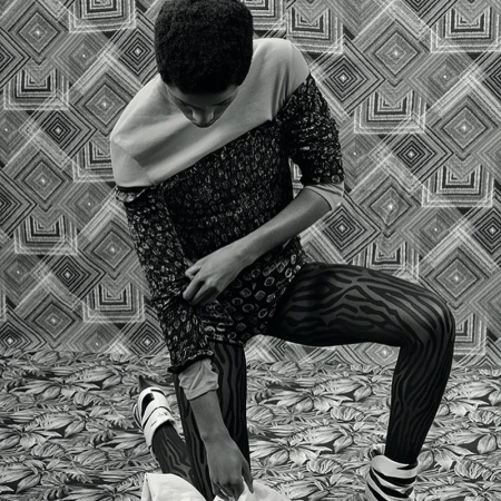 Monochrome fashion shot of a person kneeling on a patterned surface, wearing a patterned top, zebra print tights, and platform shoes.