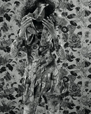 Floral fashion: A person in a floral-print outfit stands against a matching floral background, obscuring their face with floral fabric.
