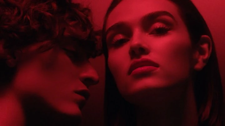 Close-up portrait of two young adult females in a dark studio setting, illuminated by vivid red lighting, emphasizing their facial features.