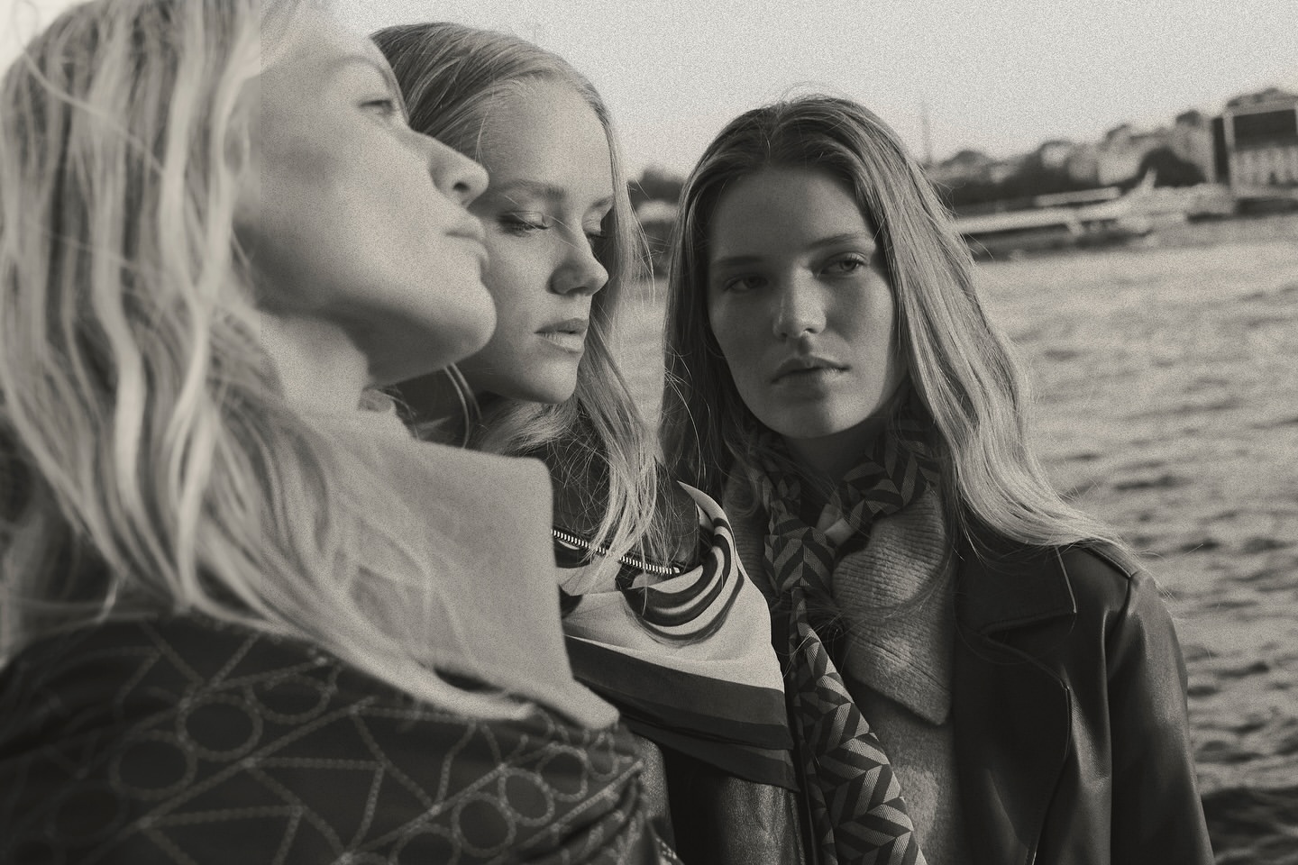 Monochrome portrait of three blonde female models outdoors by the water wearing patterned scarves and coats by Jonas Bresnan