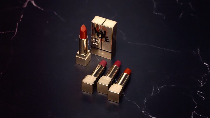 Luxury beauty product shot featuring gold YSL lipstick tubes with varying red hues, displayed on a sleek black marble surface.