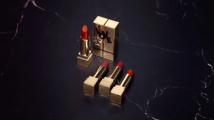 Luxury beauty product shot featuring gold YSL lipstick tubes with varying red hues, displayed on a sleek black marble surface.