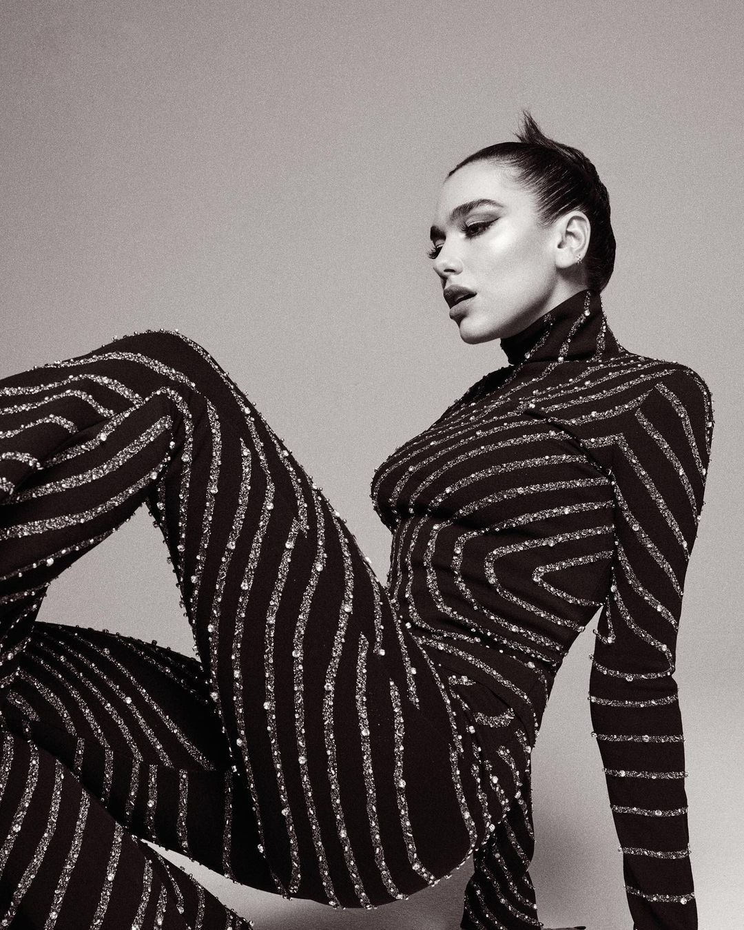 Woman in a black patterned turtleneck jumpsuit posing against a plain neutral studio backdrop
