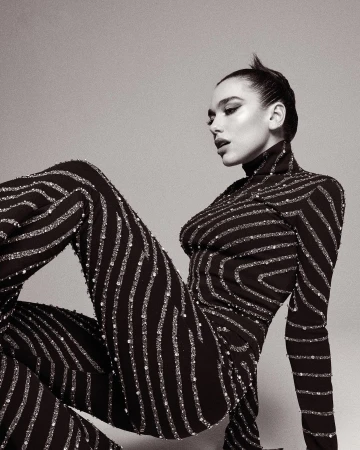 Woman in a black patterned turtleneck jumpsuit posing against a plain neutral studio backdrop