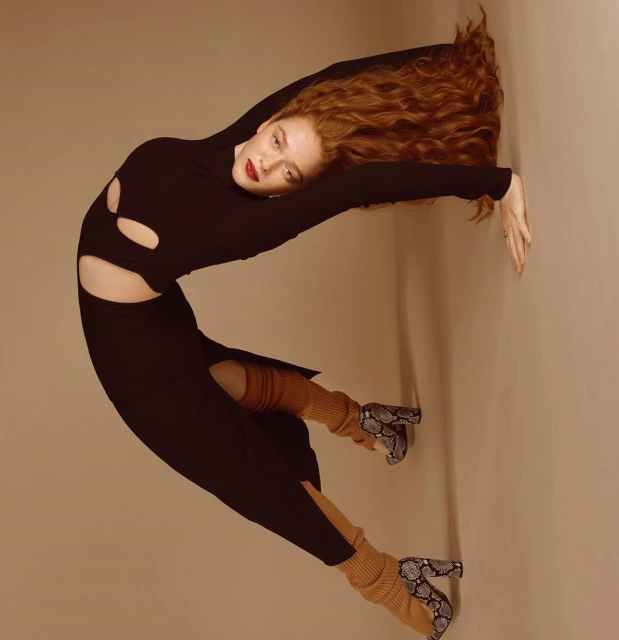 A fashionable woman in a black dress and snakeskin boots poses against a neutral background, showcasing a contemporary studio portrait.