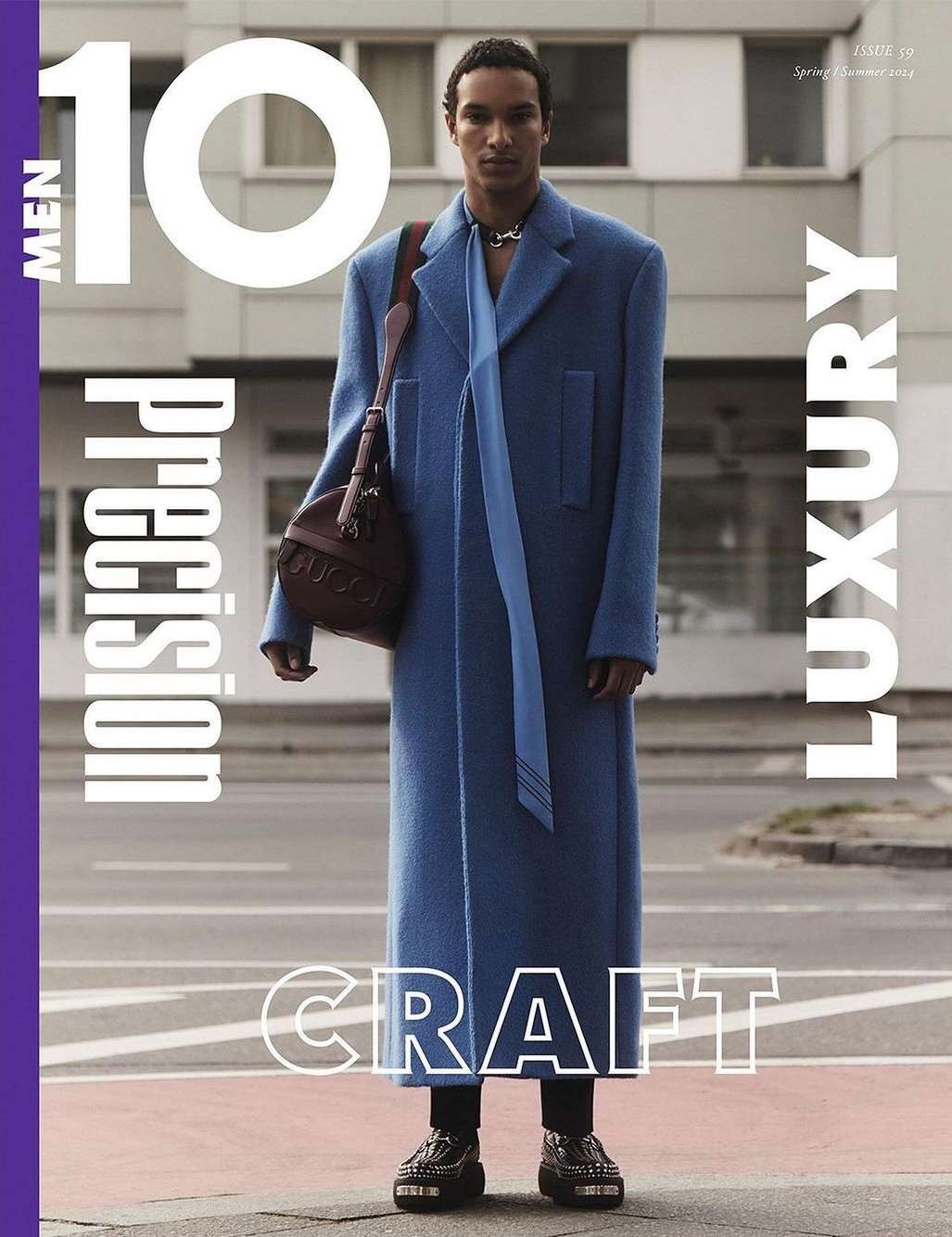 Magazine cover featuring a full-length shot of a black male model in a blue coat with a bag, standing on a city street.