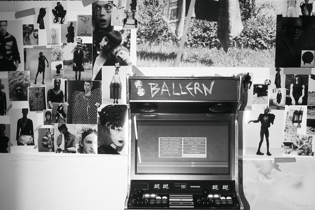 Monochrome image displays an arcade cabinet surrounded by taped photos, creating a visually rich and layered composition.