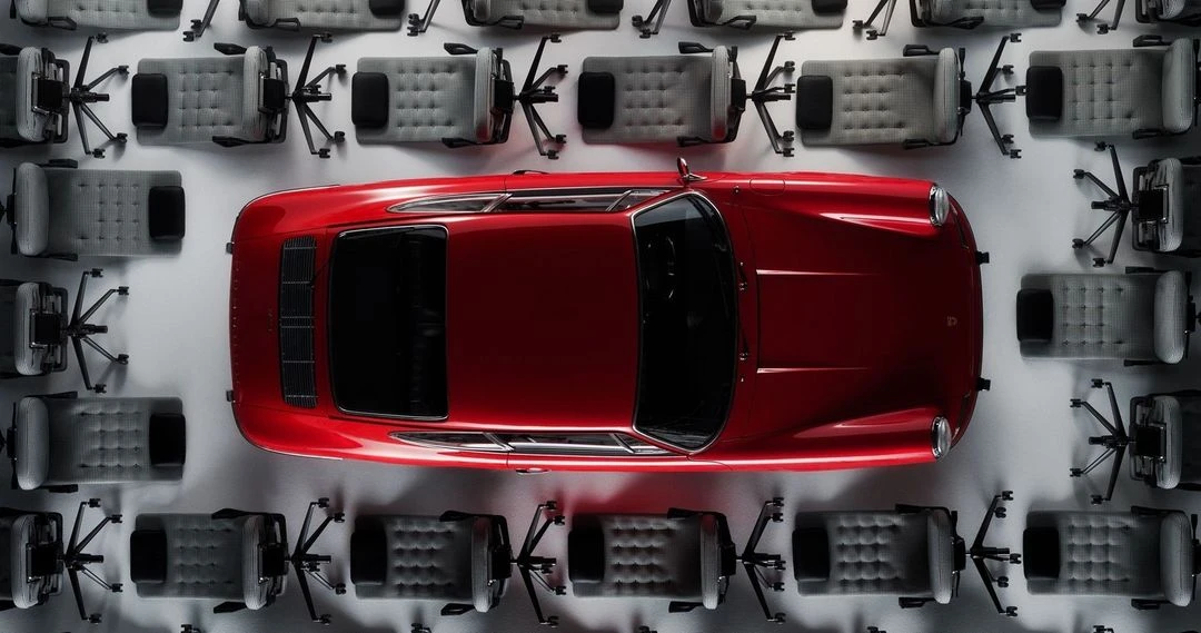 Overhead shot of a red Porsche encircled by a collection of grey office chairs on a light grey surface, creatively composed.