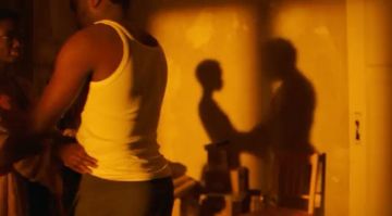 Two African adult males in a dimly lit indoor space with yellow walls and a table. The focus is on their shadows.