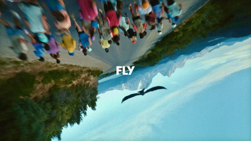 An inverted cinematic shot of a group of runners on a road with a bird flying below and the word FLY centered