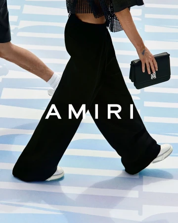 Fashion shot featuring models walking, showcasing black pants, a black handbag, and white sneakers on a light blue background. 
