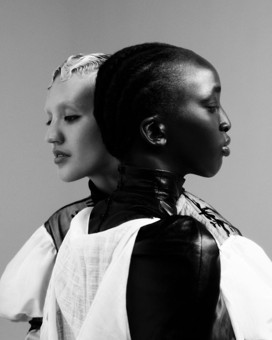 Striking black and white portrait of two fashion models of diverse ethnic backgrounds posing together in stylish outfits in a studio.