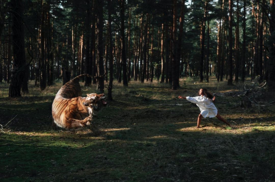 Woman in a white dress appears to confront a large tiger within a dense, dark forest; an outdoor scene with an intriguing dynamic.