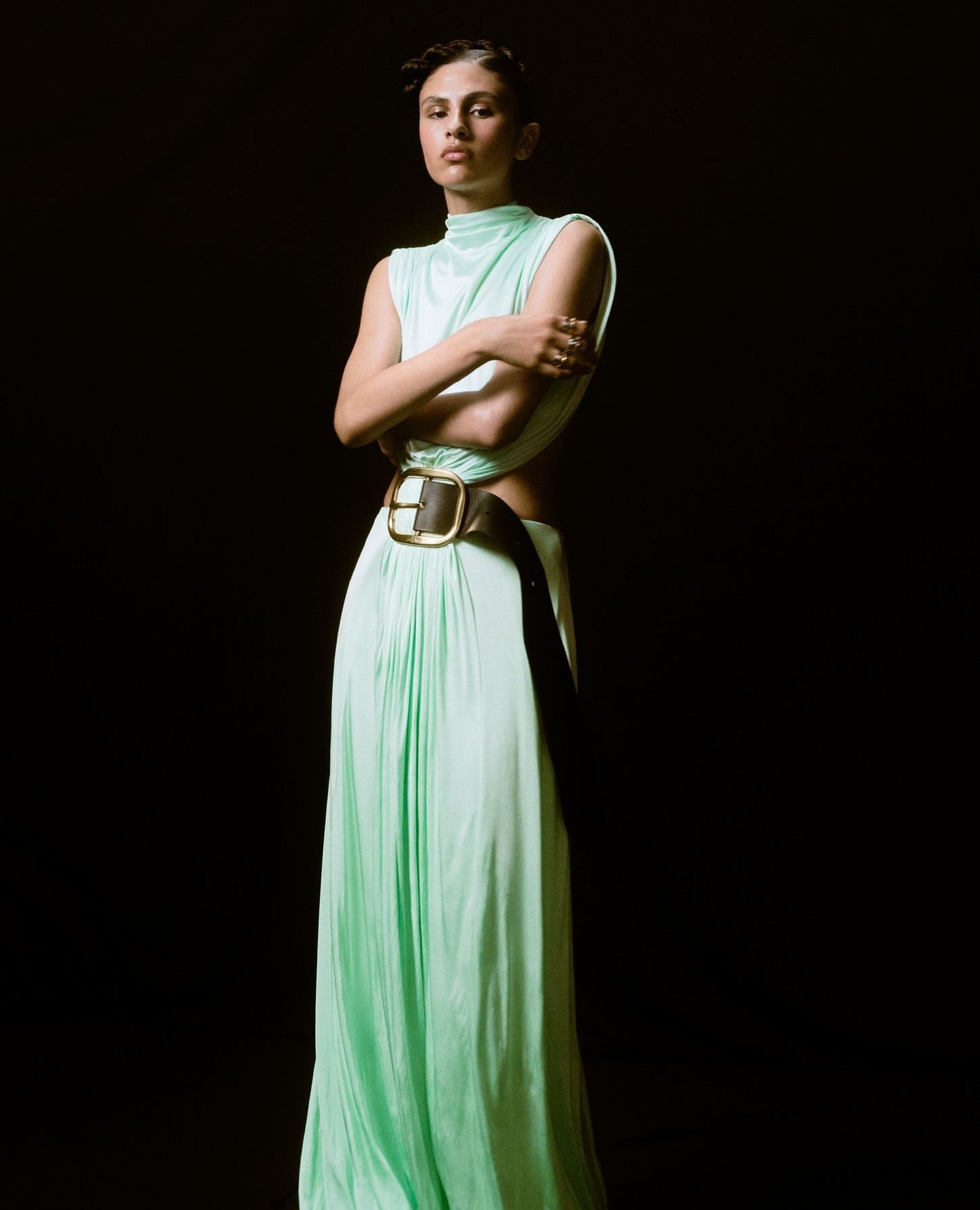 Model in mint green sleeveless gown with thick dark belt against a solid black background