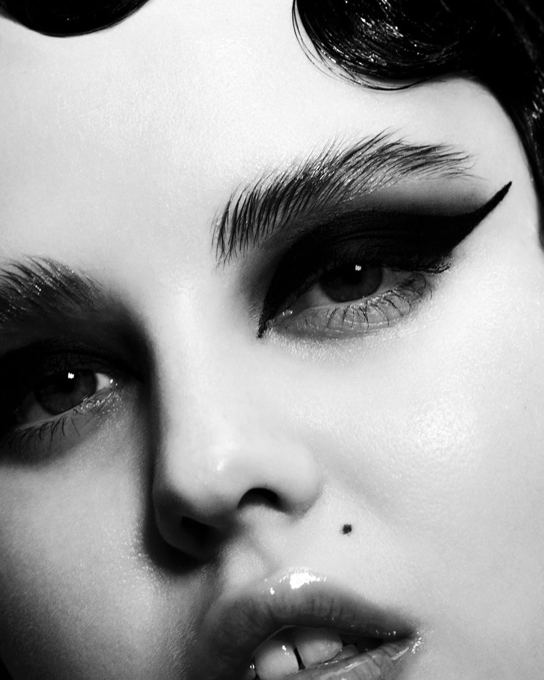 Close-up black and white portrait of a woman with heavy black eyeliner and dark, styled hair. Beauty and makeup concept.