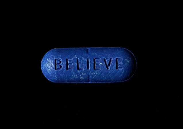 Close-up studio shot of a blue pill with the word BELIEVE on a dark backdrop, creating a minimalistic and impactful composition.