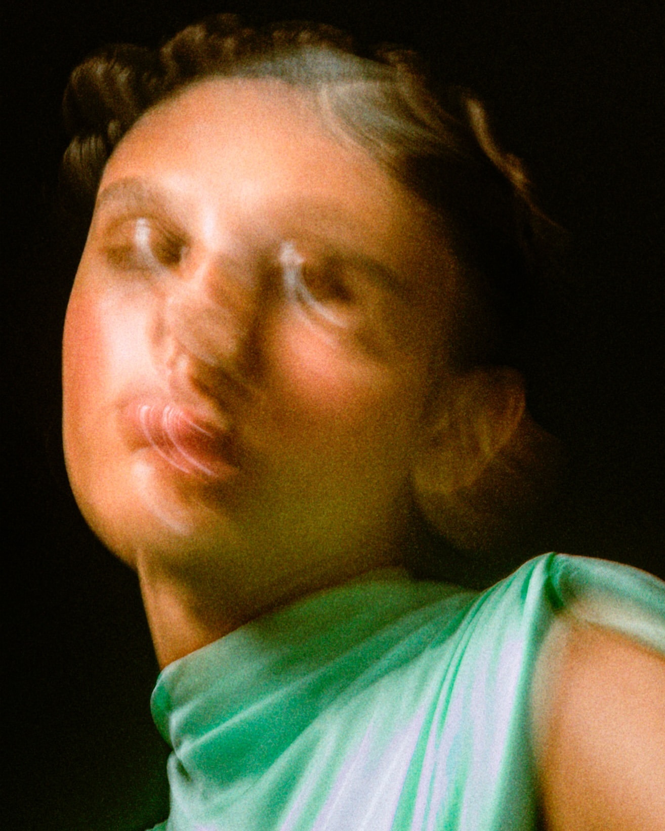 Close-up portrait of a woman with blurred motion, wearing a light green top, set against a dark background.
