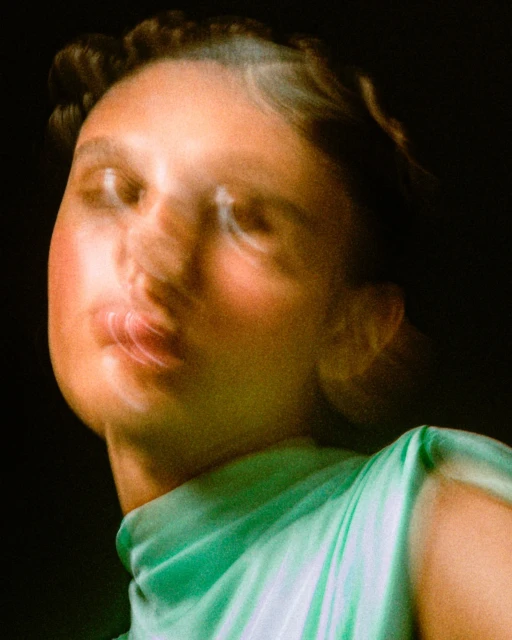Close-up portrait of a woman with blurred motion, wearing a light green top, set against a dark background.