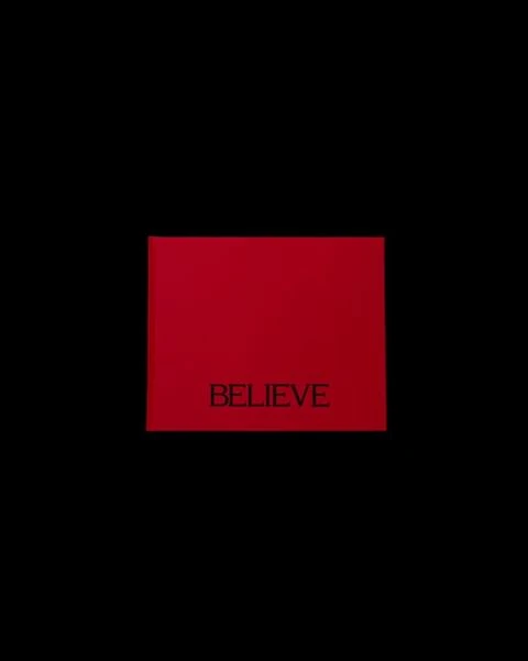 A red square centered on a black background has the word “BELIEVE” in a smaller, dark font at the center of the red shape.