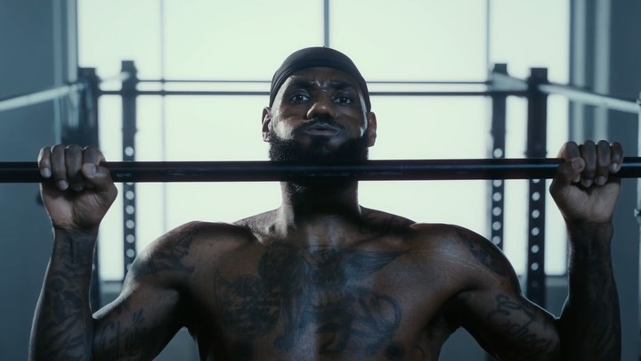Adult male athlete with tattoos lifts barbell in gym for fitness workout, wearing black beanie. Fitness concept.