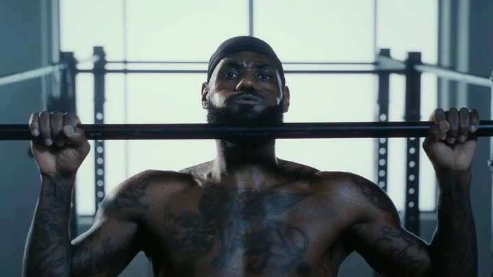 Adult male athlete with tattoos lifts barbell in gym for fitness workout, wearing black beanie. Fitness concept.