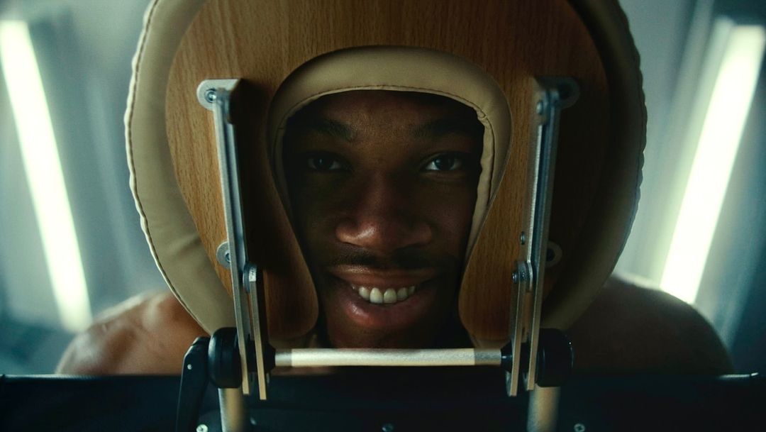 Close-up studio shot of smiling African American adult male with short dark hair and a neatly trimmed beard with massage chair.
