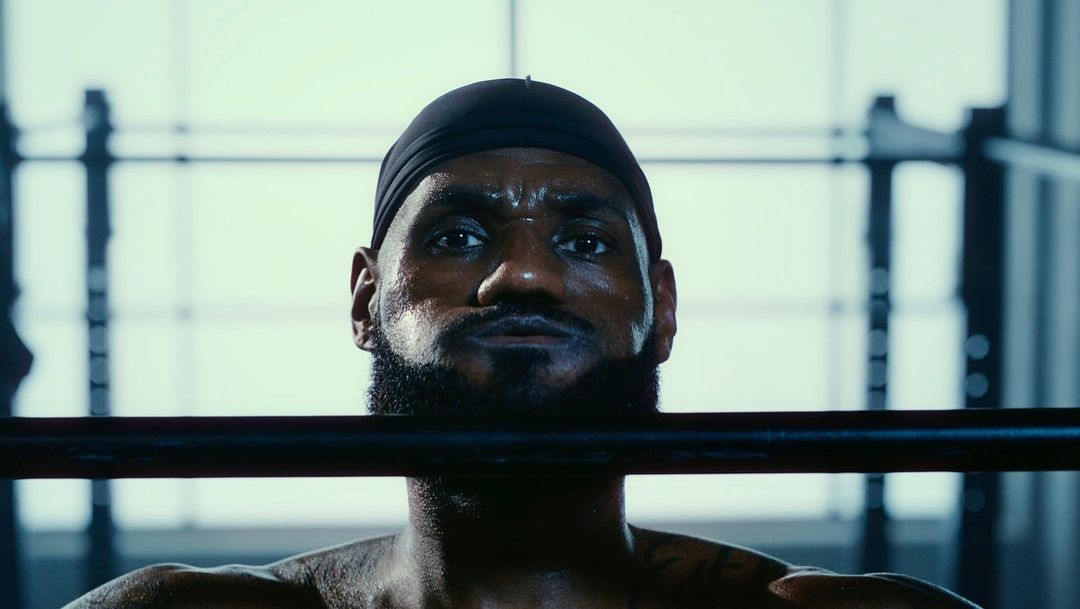 Close-up of a sweaty, determined African American adult male weightlifter wearing a black head covering in a fitness center.