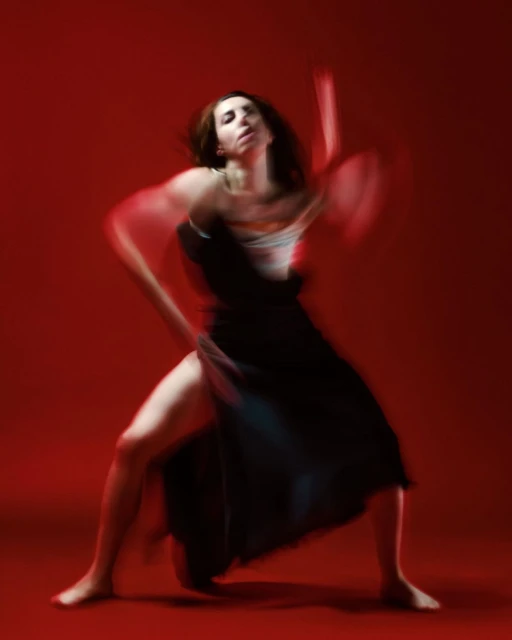 Female dancer in motion wearing a black dress and posing against a red background, capturing movement and artistic expression.
