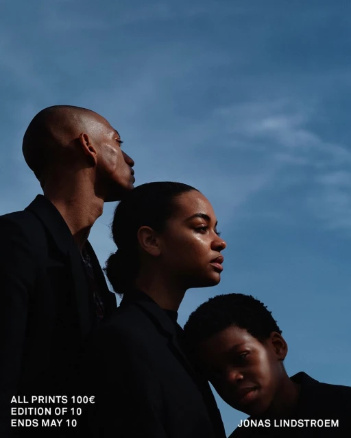 Striking portrait of three diverse individuals in dark jackets against a partly cloudy sky, highlighting fashion and photographic artistry.