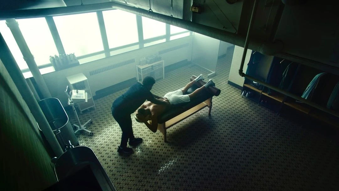 Adult male receiving a massage from an adult male wearing scrubs on a massage table in a brightly lit interior room with tile floors.