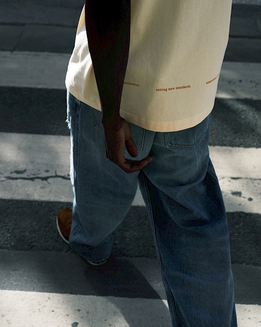 An adult crosses a zebra crossing in blue jeans and a cream T-shirt, sunlight highlights the scene, focusing on their lower body.