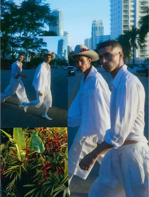Two adult males in white shirts and hats walk on a city street with palm trees, buildings, and tropical foliage in bright daylight.