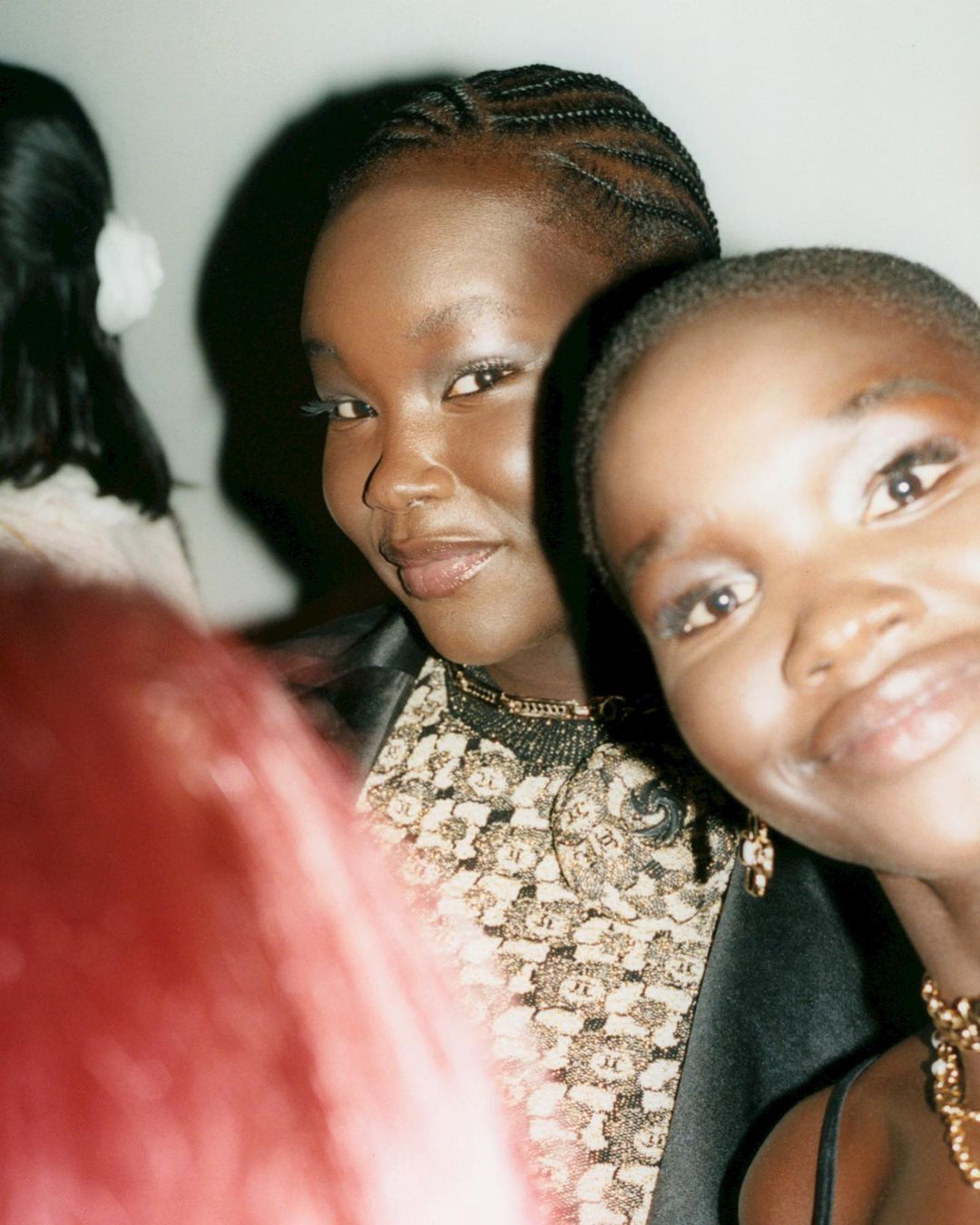 Close-up shot of two adult females with dark complexions and braided hairstyles, with one smiling and one looking directly at the camera.