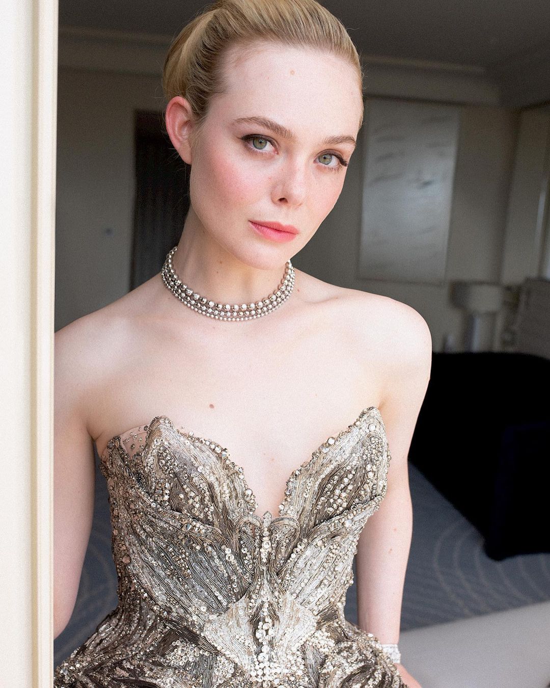 Close-up of Elle Fanning in an embellished strapless gown with a triple-strand pearl necklace, soft lighting, and light hair.