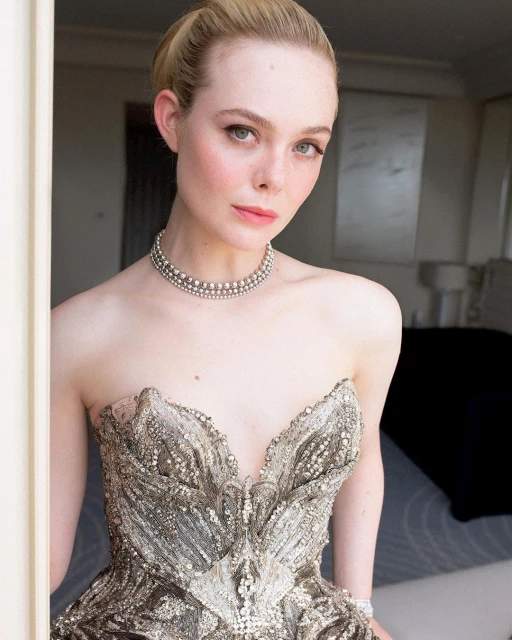 Close-up of Elle Fanning in an embellished strapless gown with a triple-strand pearl necklace, soft lighting, and light hair.