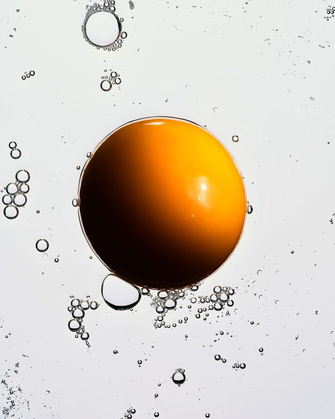 Abstract close-up of a vibrant golden sphere surrounded by translucent bubbles against a gradient white background, creating a dreamy, ethereal feel.