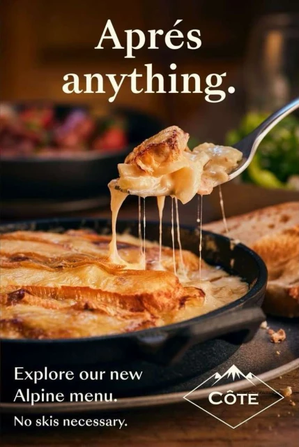 Close-up of a skillet of cheesy baked potatoes with a serving spoon holding up a portion. A restaurant advertisement for Alpine cuisine.