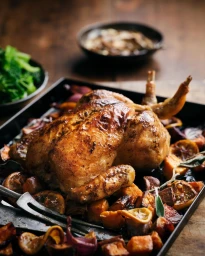 Roasted whole chicken in a baking tray with roasted lemon slices, root vegetables, and herbs on a rustic wooden table.