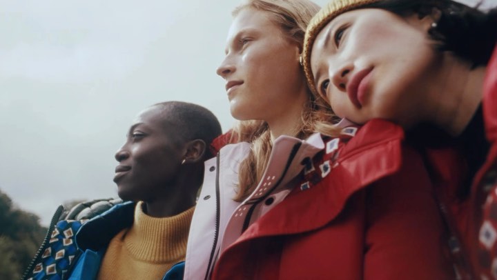 Close-up of three diverse women modeling colorful patterned winter coats against an overcast outdoor background, fashion editorial photography.