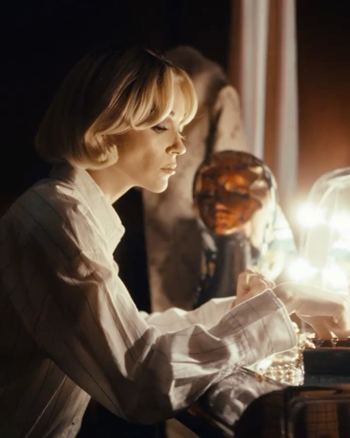 Blonde woman in white shirt focuses on craft project indoors surrounded by warm lighting, showcasing portrait angle and soft focus.