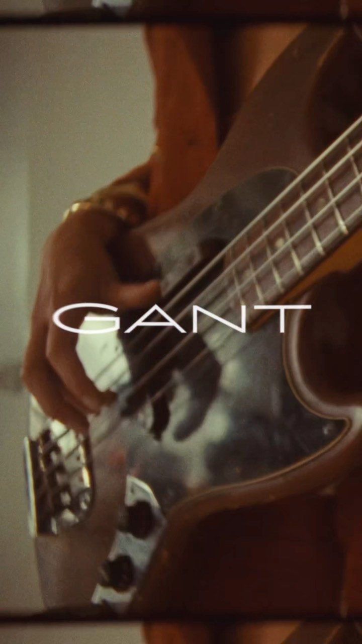 Close-up of a musician playing an electric bass guitar with the brand name GANT overlaid, shot with a shallow depth of field.