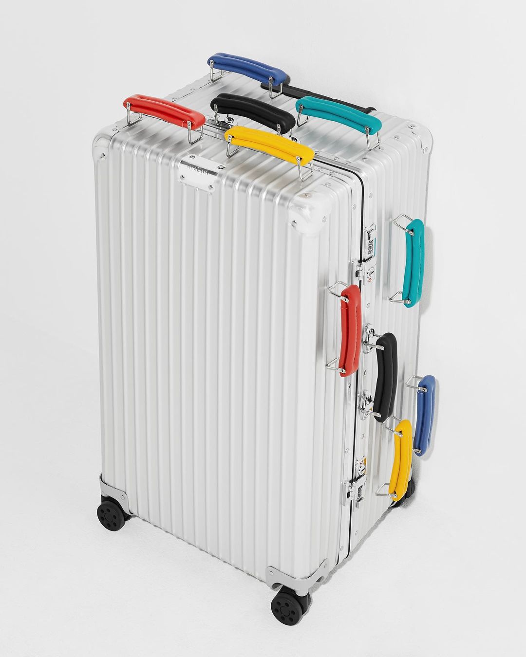 Silver rolling suitcase with multiple colorful handles on a white background in a product shot. Travel luggage and storage.
