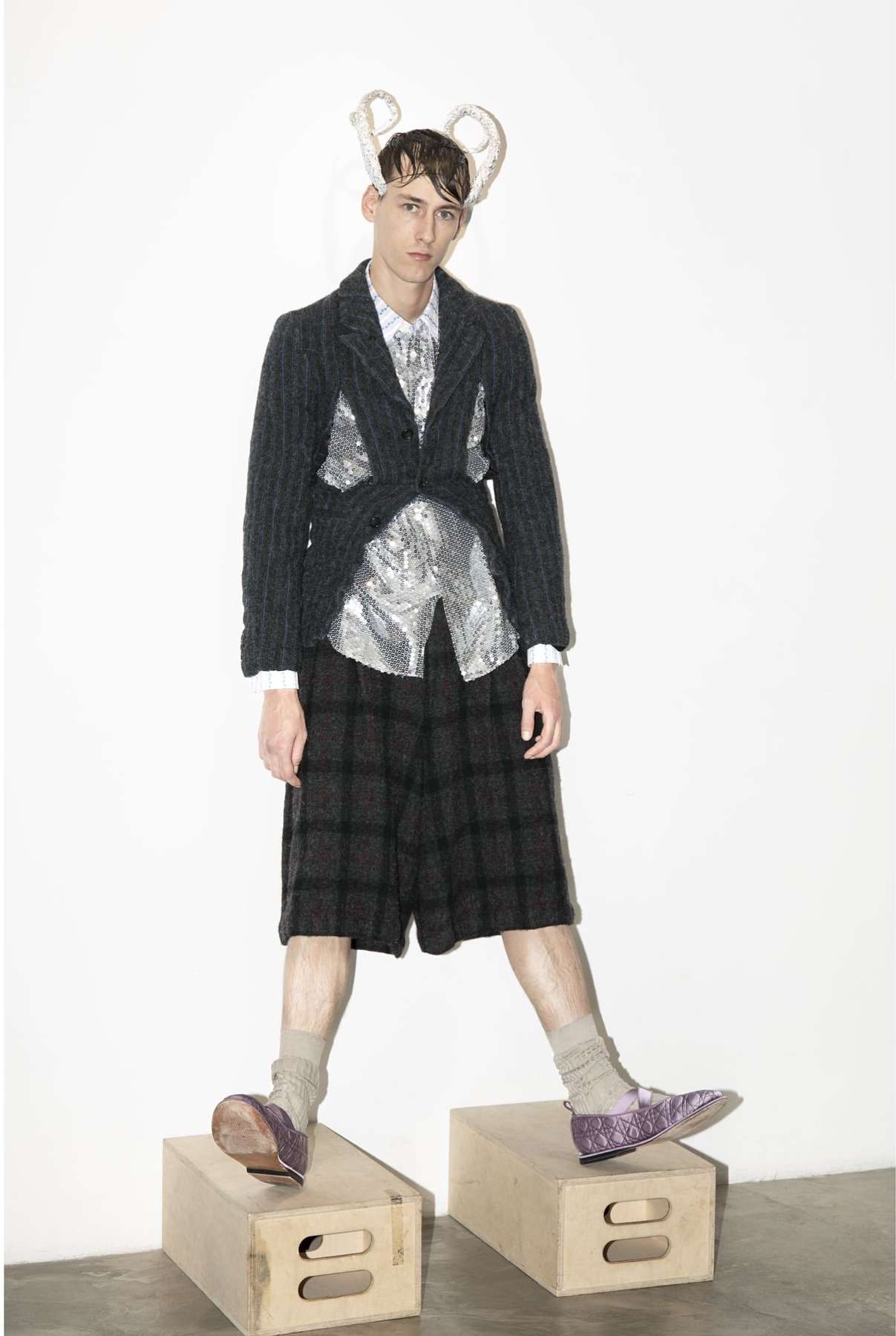 Full shot of a man in a fashion blazer, shorts, socks, and shoes standing on wooden boxes with a white background in a studio setting.