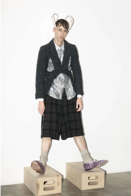 Full shot of a man in a fashion blazer, shorts, socks, and shoes standing on wooden boxes with a white background in a studio setting.