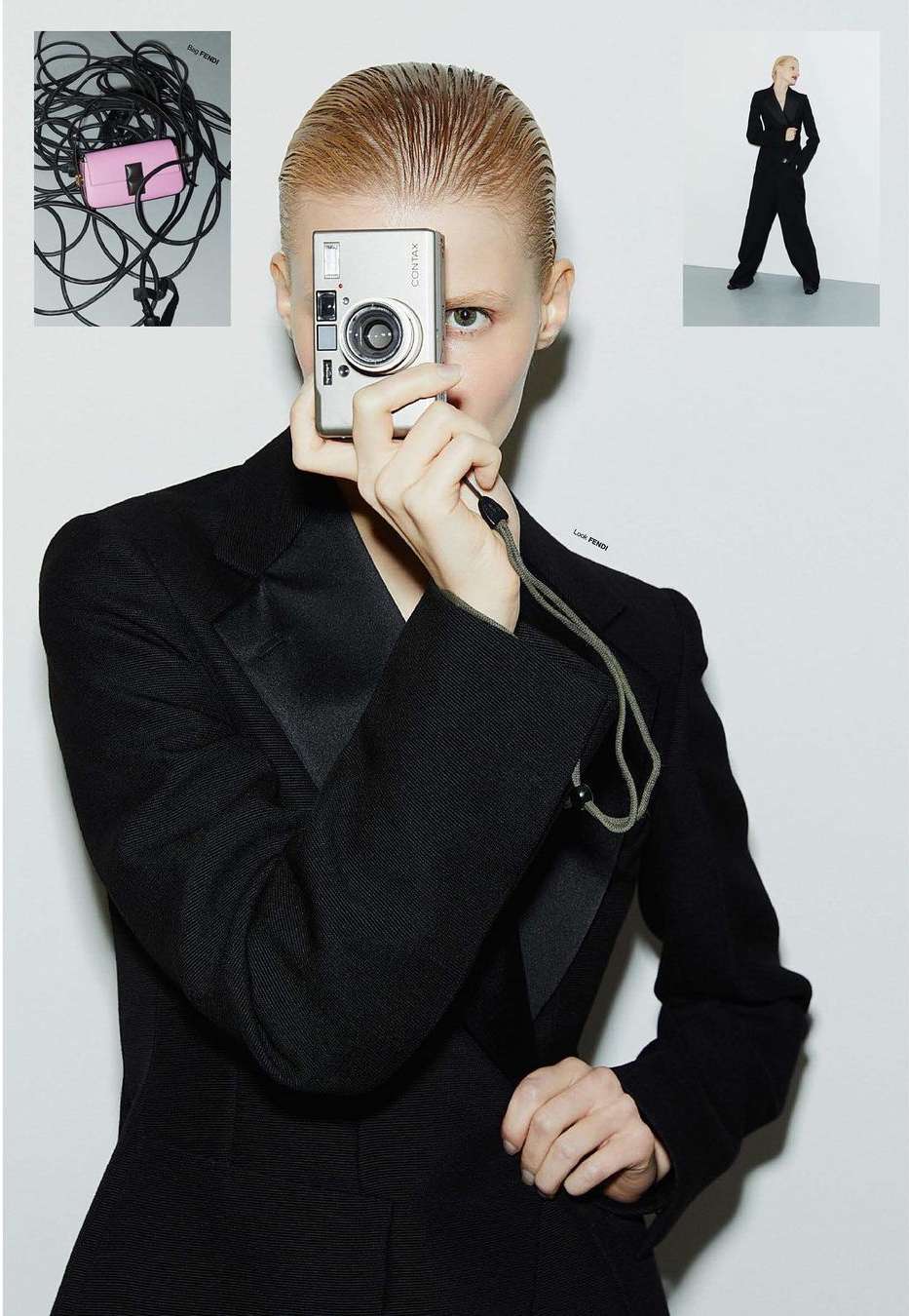 Adult woman in black suit holding silver camera in front of her face in a photo studio with other photography equipment visible.