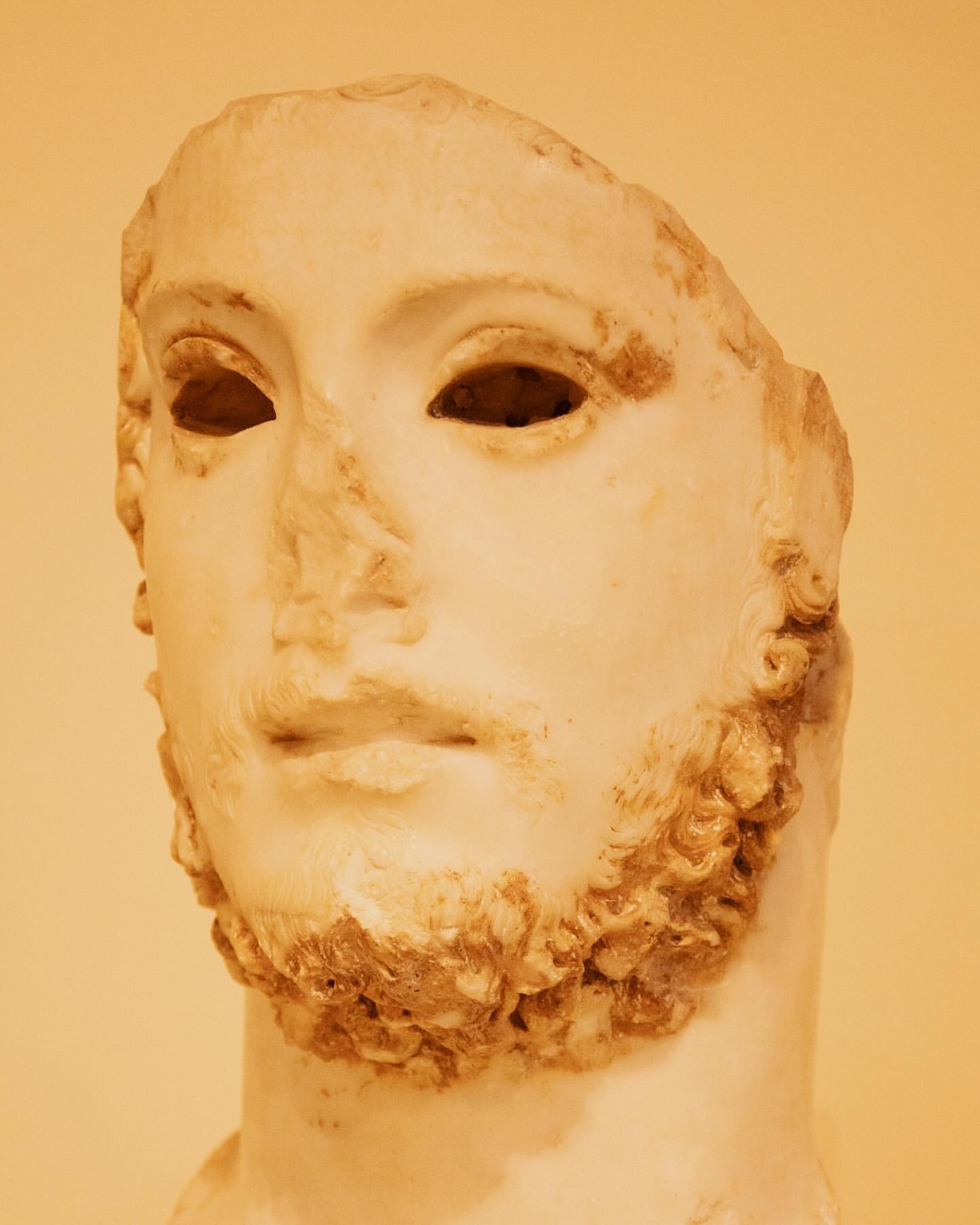 Close-up studio shot of a marble sculpture fragment depicting a man's head with a beard against a neutral background.