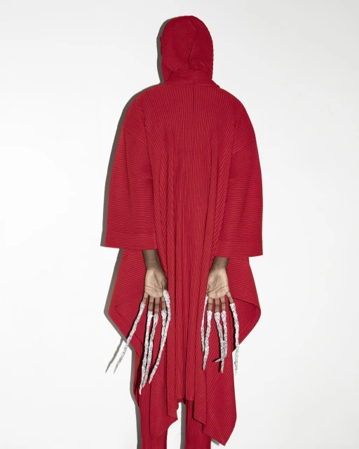 Person in red hooded robe facing away, showing extra-long fingernails, against a white background. Fashion and beauty concept.